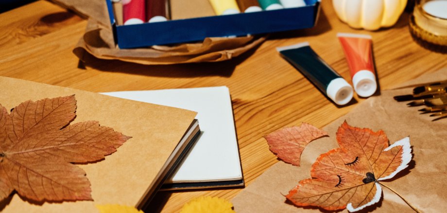 Tisch mit Bastelmaterialien, Schere Papier und bunte Herbstblätter