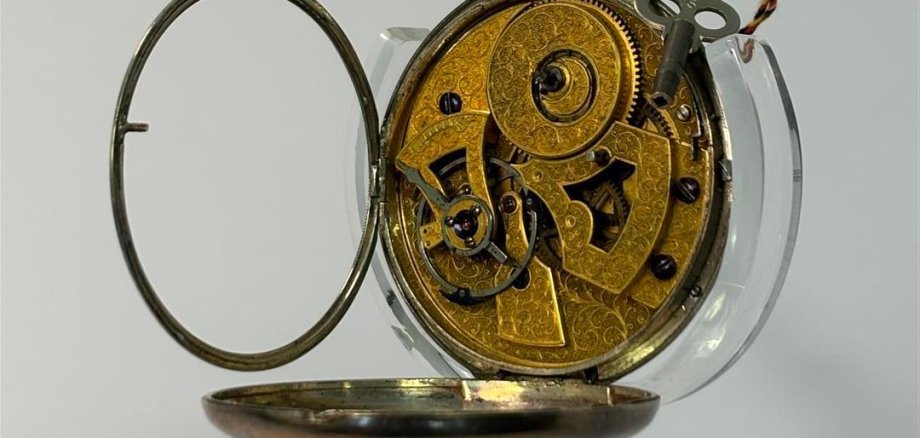 Fotografie einer vermutlich aus der Schweiz stammenden Taschenuhr im geöffneten Zustand mit Blick auf das reich verzierte Uhrwerk.